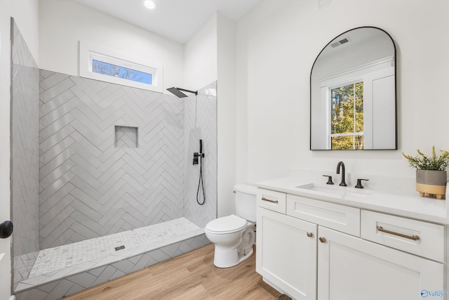 bathroom with toilet, a tile shower, vanity, and wood-type flooring