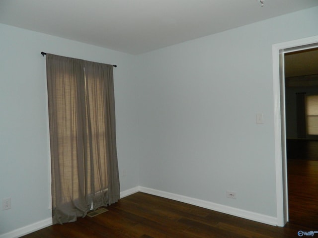 unfurnished room with visible vents, dark wood finished floors, and baseboards