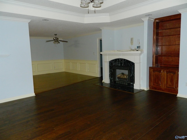 unfurnished living room featuring a raised ceiling, ceiling fan, a premium fireplace, wood-type flooring, and crown molding