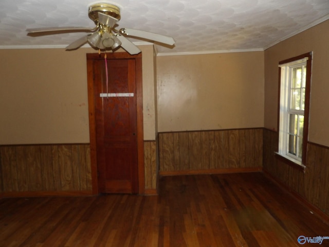 spare room featuring ornamental molding, wooden walls, ceiling fan, and dark hardwood / wood-style flooring