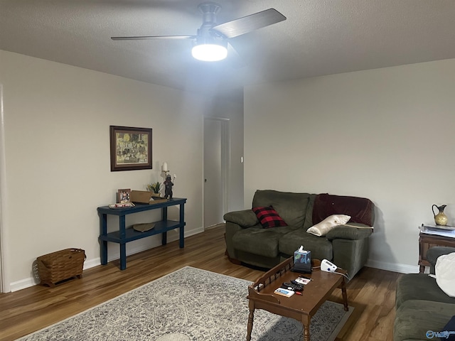 living area featuring a ceiling fan, a textured ceiling, baseboards, and wood finished floors