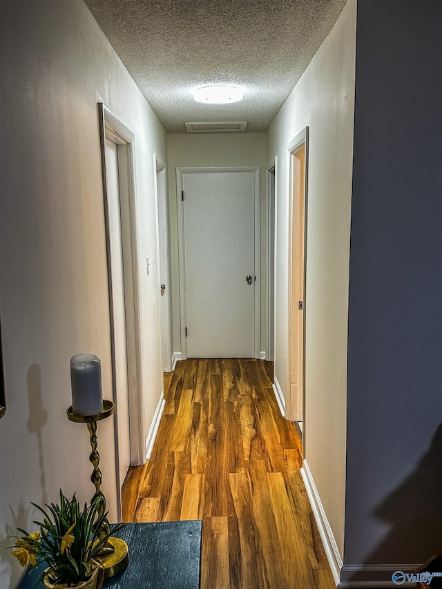 hall with baseboards, a textured ceiling, visible vents, and wood finished floors