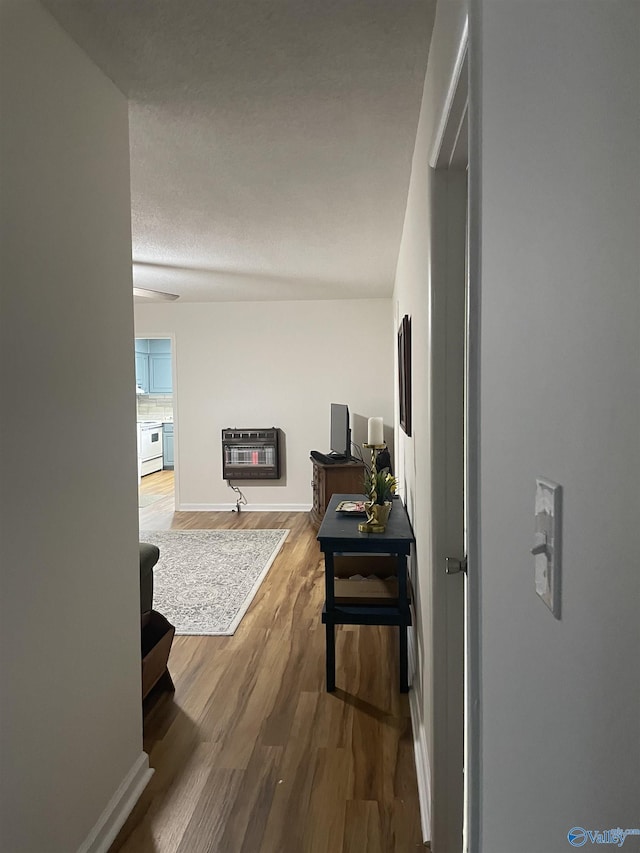 corridor featuring baseboards, wood finished floors, and heating unit