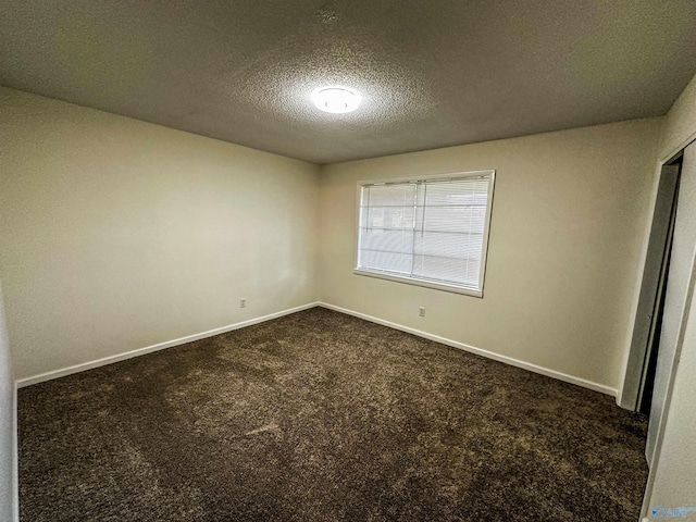 empty room with a textured ceiling, dark colored carpet, and baseboards