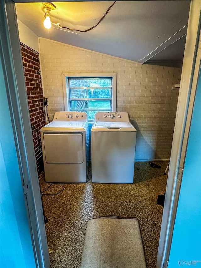 washroom featuring laundry area, brick wall, and washing machine and dryer