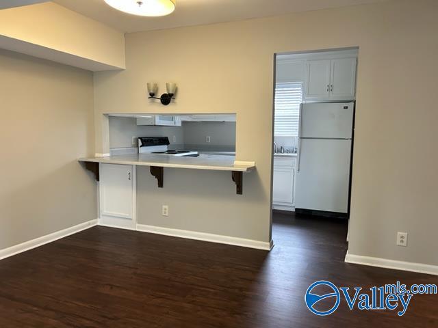 kitchen with freestanding refrigerator, baseboards, range with electric stovetop, and a kitchen bar