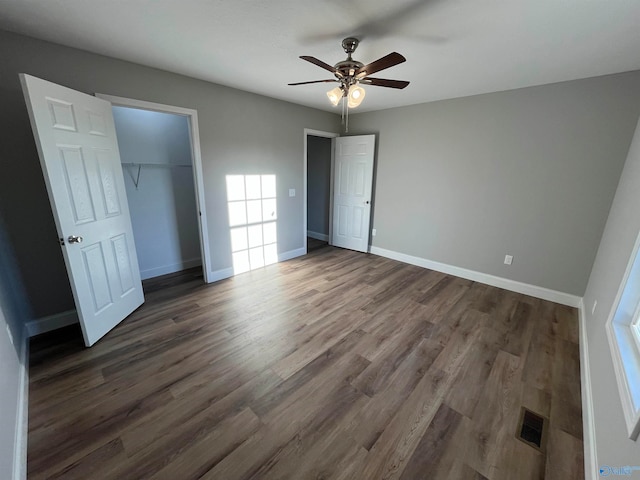 unfurnished bedroom with a closet, dark wood-type flooring, a walk in closet, and ceiling fan