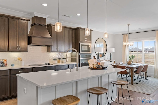 kitchen featuring appliances with stainless steel finishes, a center island with sink, and hanging light fixtures