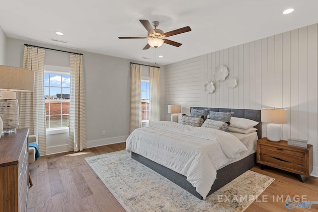 bedroom with ceiling fan, wood walls, and hardwood / wood-style flooring