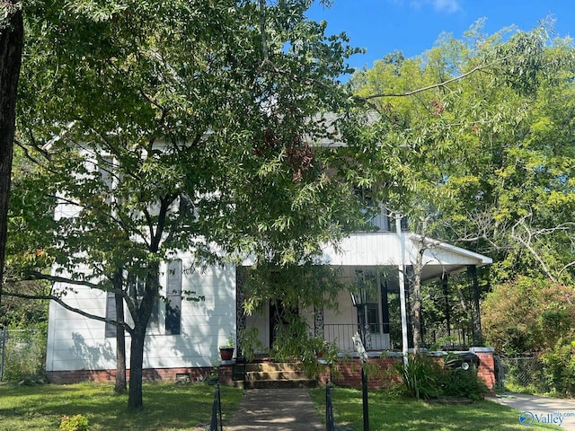 view of property hidden behind natural elements with covered porch and a front lawn