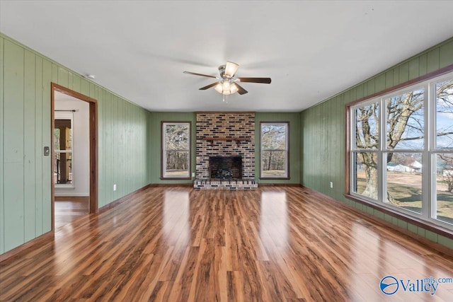 unfurnished living room with ceiling fan, wood-type flooring, a fireplace, and plenty of natural light