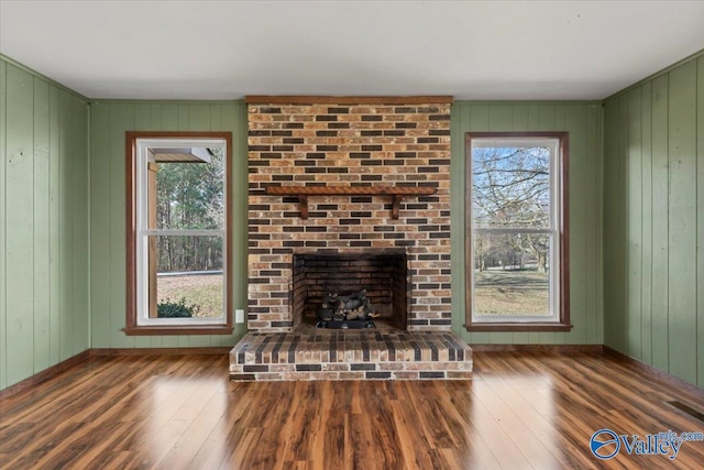 unfurnished living room featuring a brick fireplace, a wealth of natural light, and dark hardwood / wood-style flooring