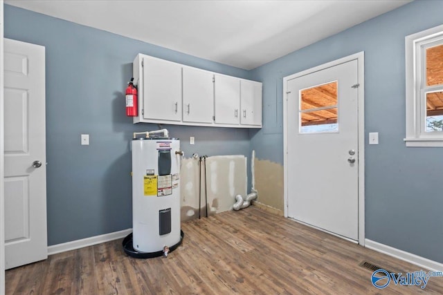 laundry room with dark wood-type flooring, cabinets, and electric water heater