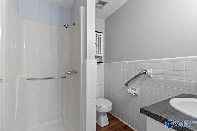 bathroom featuring a shower, a textured ceiling, tile walls, vanity, and hardwood / wood-style floors