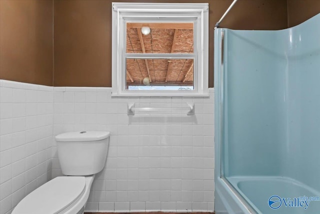 bathroom with tile walls, shower / bath combination with glass door, and toilet