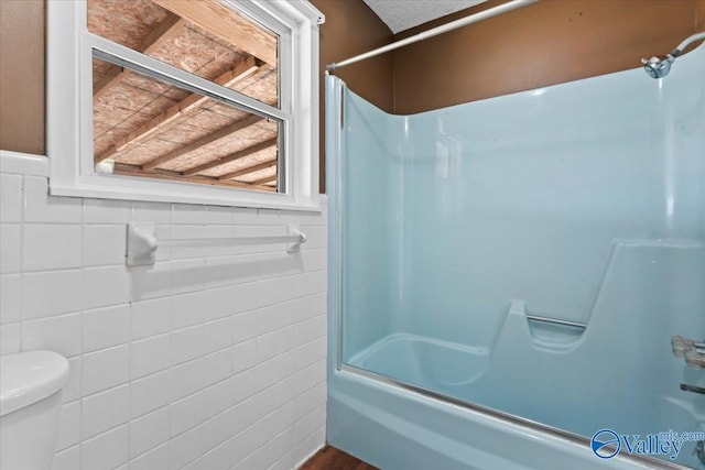 bathroom with enclosed tub / shower combo, toilet, and tile walls