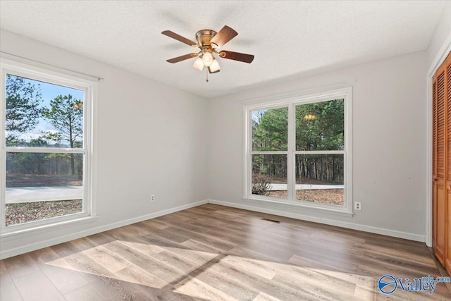 spare room featuring ceiling fan, plenty of natural light, a textured ceiling, and light hardwood / wood-style flooring