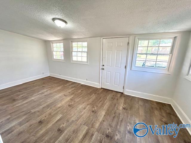 unfurnished room with a textured ceiling, wood finished floors, plenty of natural light, and baseboards