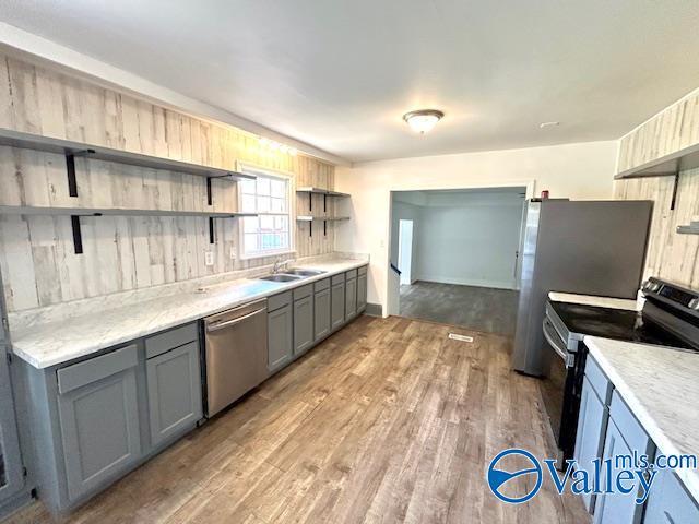 kitchen featuring range with electric cooktop, stainless steel dishwasher, open shelves, a sink, and gray cabinets