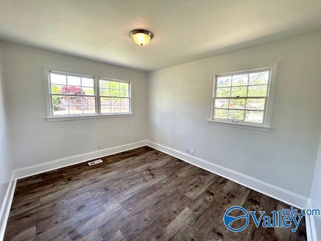 empty room featuring dark wood-type flooring, visible vents, and baseboards