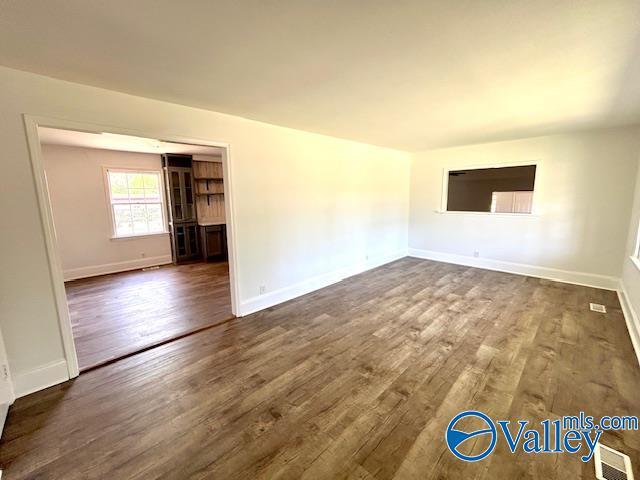 unfurnished living room featuring dark wood-style floors, visible vents, and baseboards
