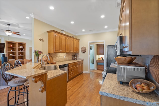 kitchen featuring a kitchen bar, ornamental molding, a peninsula, stainless steel appliances, and a sink