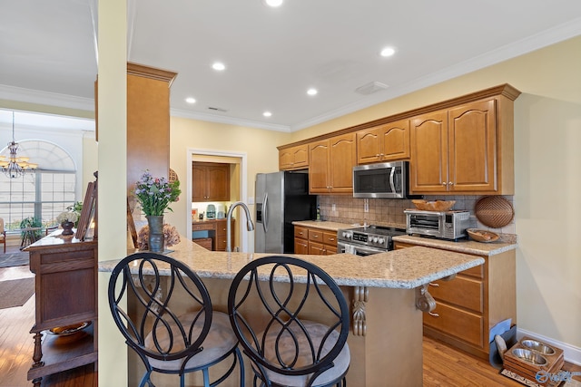 kitchen with light wood-style flooring, stainless steel appliances, a kitchen bar, crown molding, and backsplash