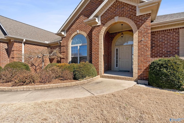 entrance to property featuring brick siding and a shingled roof