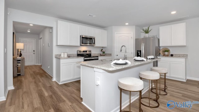 kitchen featuring sink, a kitchen island with sink, stainless steel appliances, white cabinets, and a kitchen bar