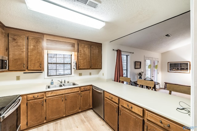 kitchen with sink, a textured ceiling, kitchen peninsula, stainless steel appliances, and light hardwood / wood-style floors