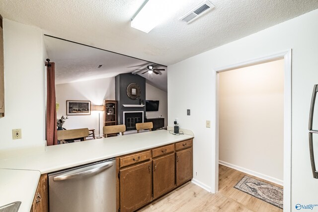 kitchen with a large fireplace, stainless steel dishwasher, ceiling fan, kitchen peninsula, and light wood-type flooring