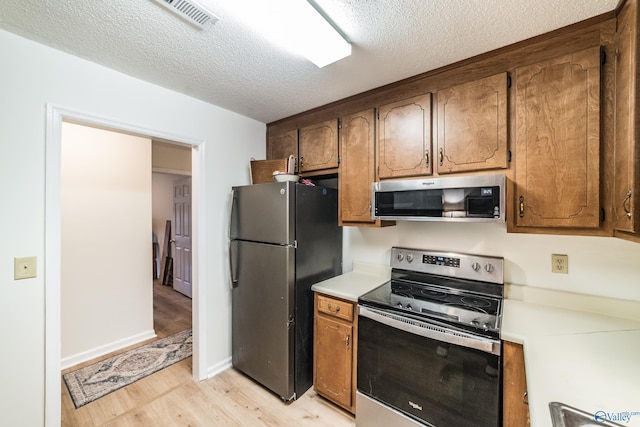 kitchen with light wood-type flooring, a textured ceiling, and appliances with stainless steel finishes