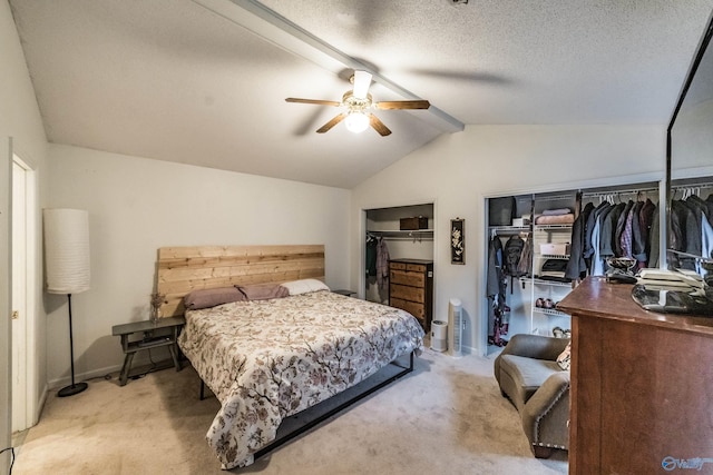 carpeted bedroom featuring ceiling fan, a textured ceiling, vaulted ceiling, and multiple closets