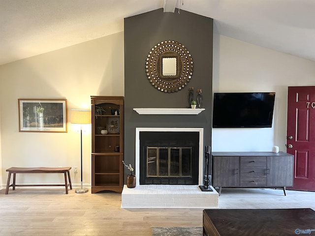 living room featuring vaulted ceiling with beams, a fireplace, and light hardwood / wood-style flooring