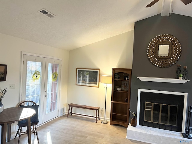 foyer with french doors, vaulted ceiling with beams, light wood-type flooring, ceiling fan, and a fireplace