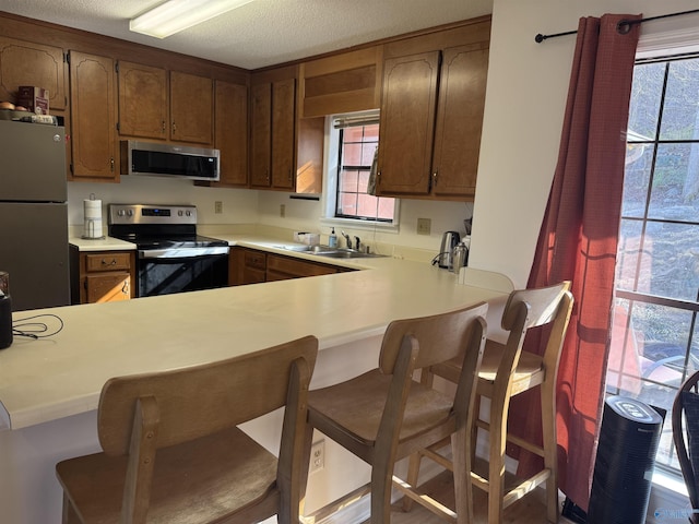 kitchen with appliances with stainless steel finishes, a wealth of natural light, a kitchen breakfast bar, and kitchen peninsula