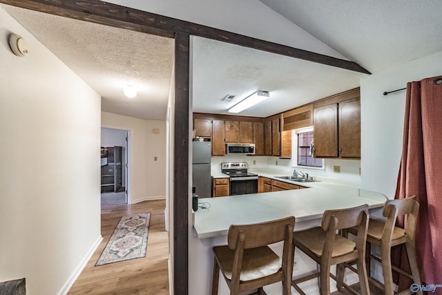 kitchen featuring appliances with stainless steel finishes, a breakfast bar, sink, kitchen peninsula, and light wood-type flooring