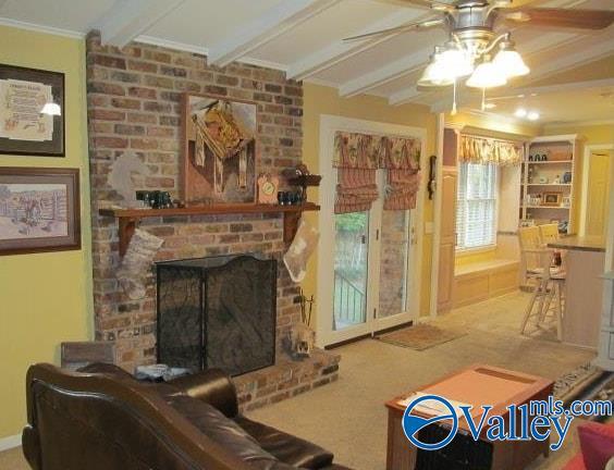 carpeted living room featuring ceiling fan, a fireplace, ornamental molding, and beamed ceiling