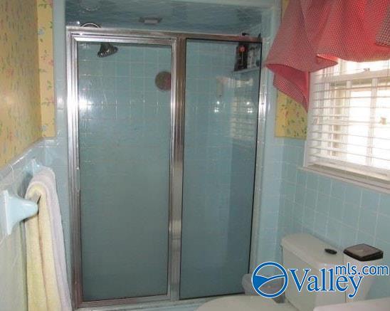 bathroom featuring tile walls, a shower with door, and toilet