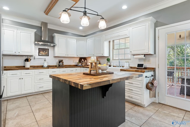 kitchen featuring crown molding, hanging light fixtures, wooden counters, white cabinets, and wall chimney range hood