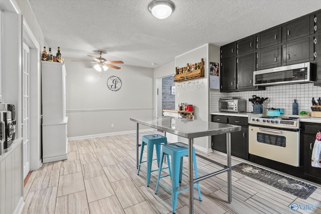 kitchen with dark cabinets, light countertops, electric stove, stainless steel microwave, and tasteful backsplash