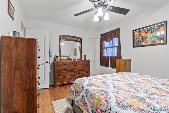 bedroom with light wood finished floors, visible vents, a textured ceiling, and a ceiling fan