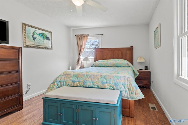 bedroom featuring a ceiling fan, wood finished floors, visible vents, and baseboards