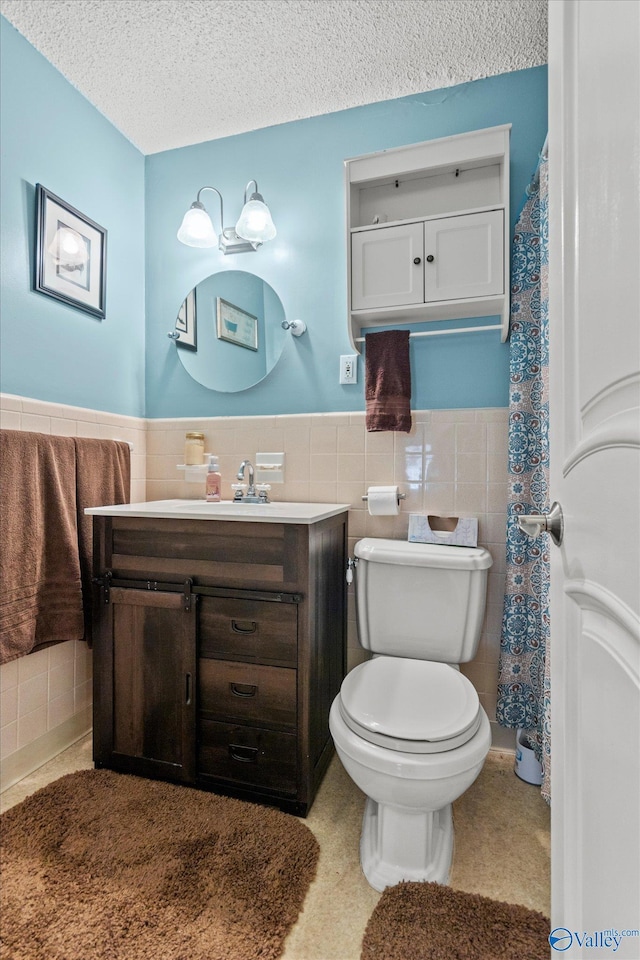 bathroom featuring tile walls, a wainscoted wall, toilet, a textured ceiling, and vanity