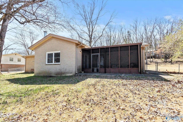 back of property with a gate, fence, a yard, a sunroom, and brick siding