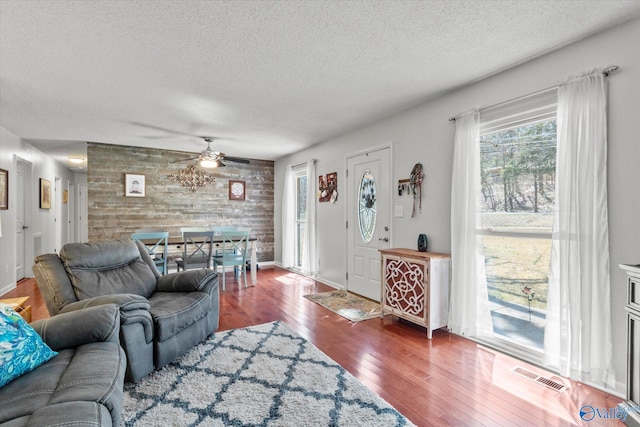 living area with visible vents, an accent wall, ceiling fan, a textured ceiling, and wood-type flooring