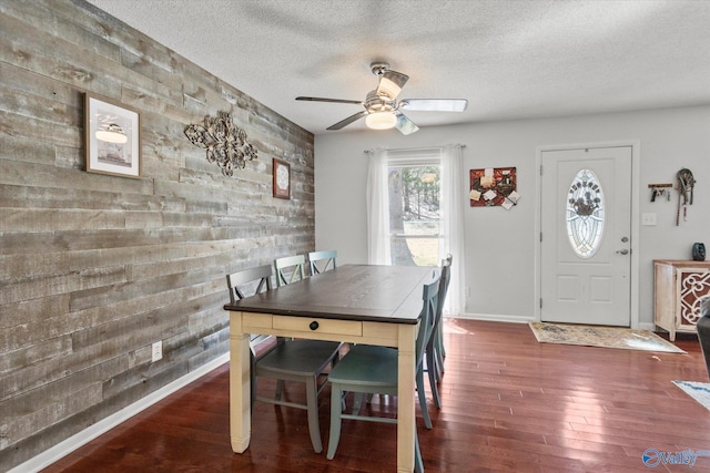 dining space featuring a ceiling fan, a textured ceiling, wood finished floors, baseboards, and an accent wall