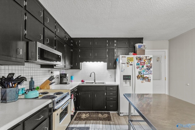 kitchen featuring decorative backsplash, white appliances, dark cabinetry, and a sink