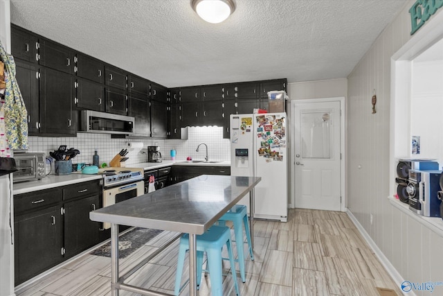 kitchen featuring a sink, a textured ceiling, dark cabinetry, white appliances, and decorative backsplash