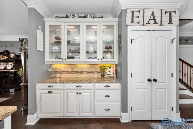 bar with light stone counters, dark hardwood / wood-style floors, backsplash, white cabinets, and ornamental molding